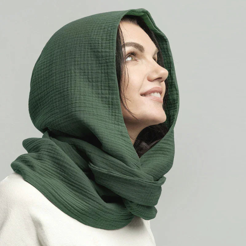 Woman wearing a textured dark green hooded scarf looking upward with a soft smile
