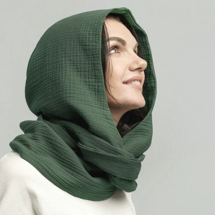 Woman wearing a textured dark green hooded scarf looking upward with a soft smile