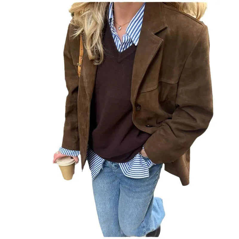 Woman wearing brown suede jacket, dark sweater, striped shirt, blue jeans, holding coffee cup