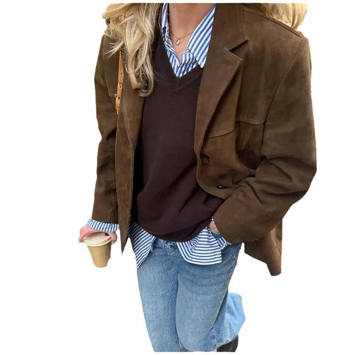Woman wearing brown suede jacket, dark sweater, striped shirt, blue jeans, holding coffee cup
