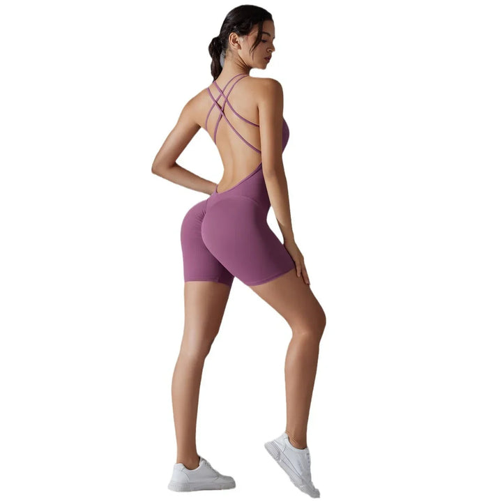 Woman wearing mauve seamless open-back athletic romper with criss-cross straps and white sneakers