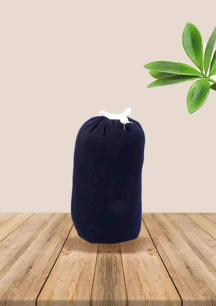 Dark blue drawstring bag on wooden table with beige background and green plant leaves