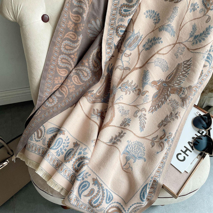 Elegant beige shawl with intricate blue and brown paisley and bird patterns draped on tufted chair
