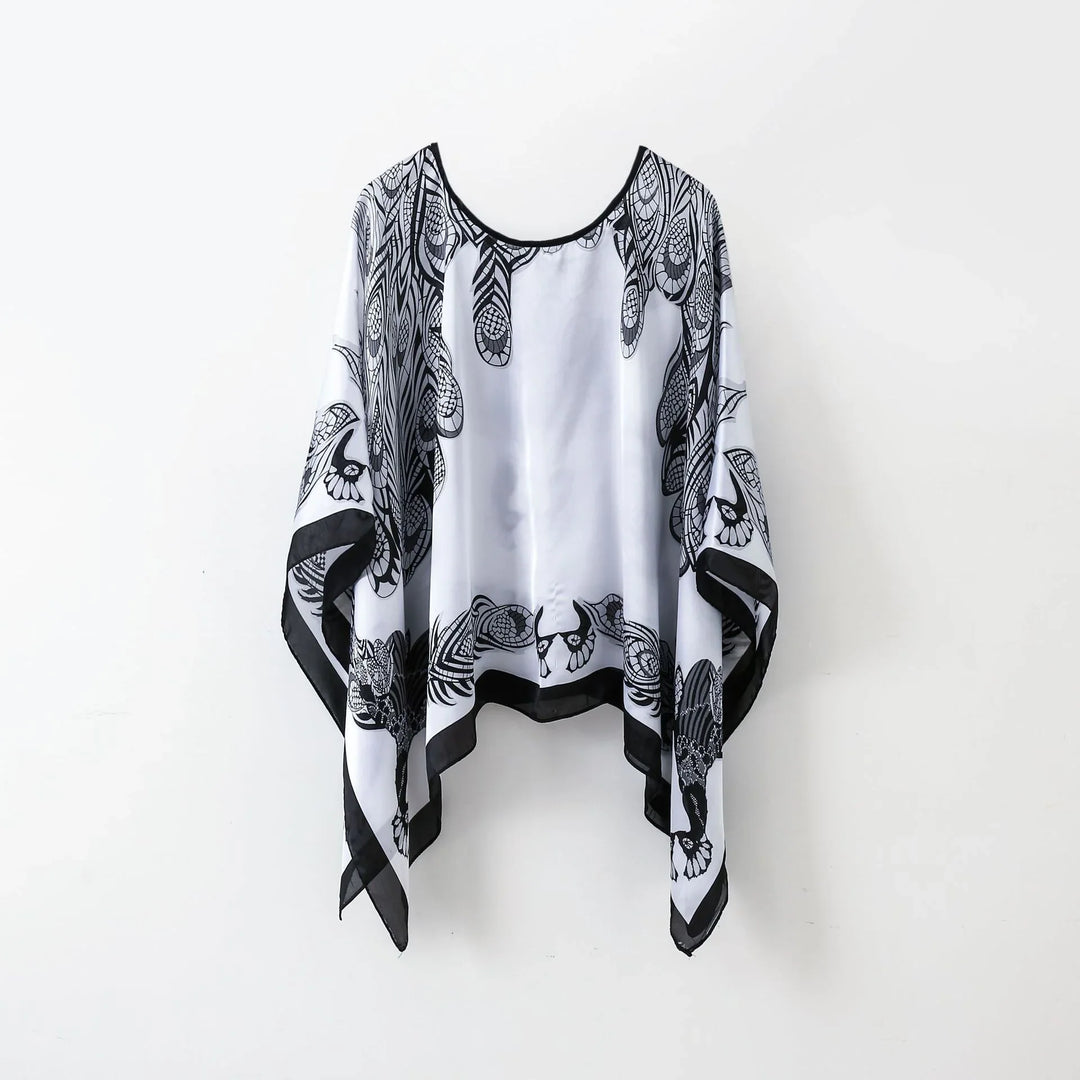 Black and white silk poncho with intricate feather and floral pattern, hanging on white background
