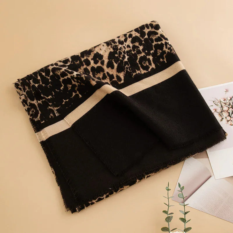 Folded black and beige leopard print scarf with fringe edges on beige surface