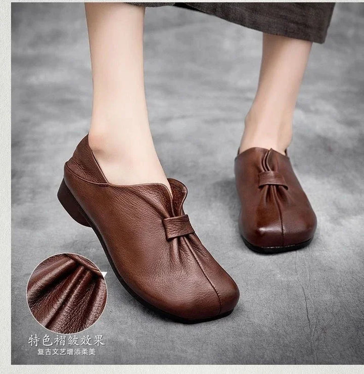 brown leather slip-on shoes with pleated front detail on gray surface