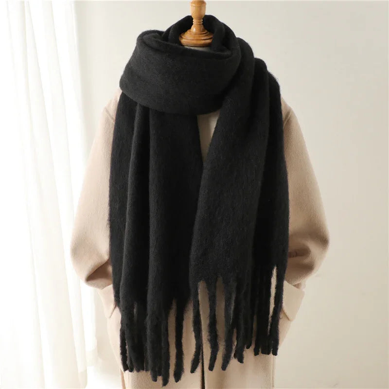 Black oversized fringed wool scarf on beige coat displayed on wooden mannequin