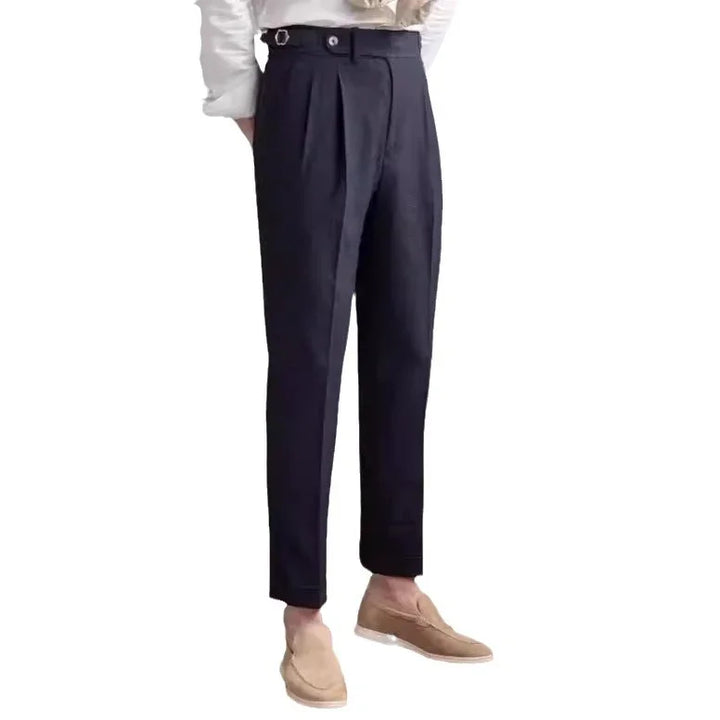 Men's black tapered dress pants with pleats, button strap detail, paired with beige loafers