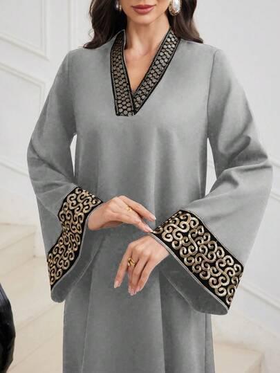 Woman wearing grey long-sleeve dress with black and gold embroidered cuffs and neckline