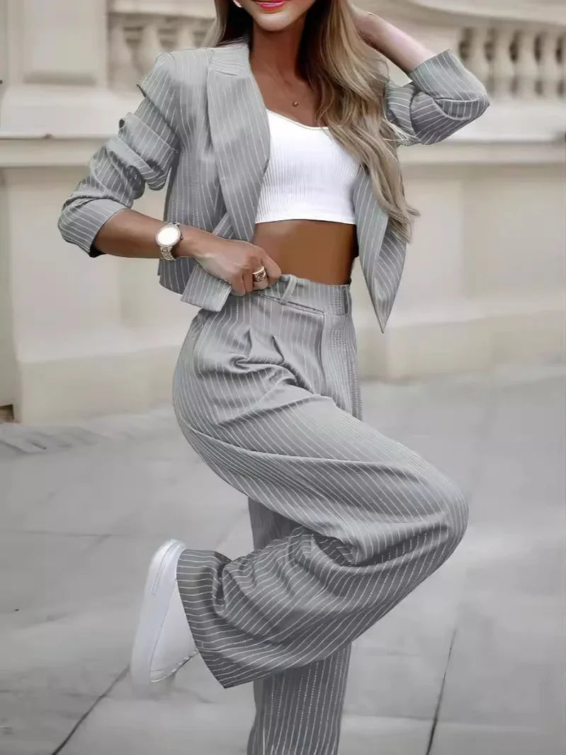 Woman wearing grey pinstripe suit with cropped blazer, high-waisted pants, white crop top, and white sneakers
