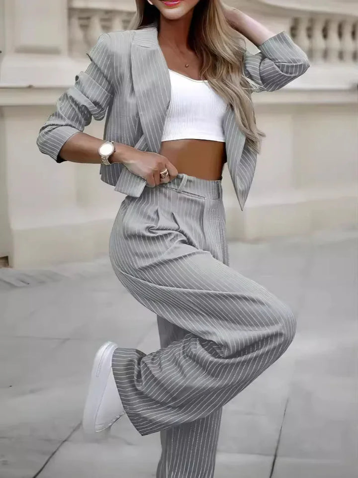 Woman wearing grey pinstripe suit with cropped blazer, high-waisted pants, white crop top, and white sneakers