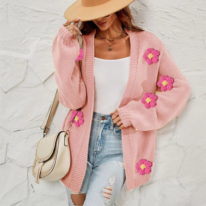 Woman wearing pink knit cardigan with floral patches, white tank top, ripped jeans, beige hat, and cream shoulder bag