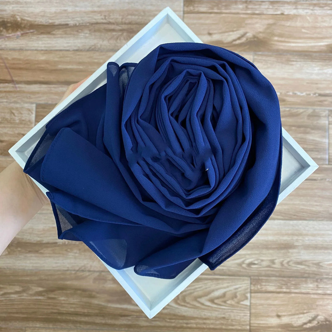 Hand holding white tray with neatly folded navy blue chiffon fabric on wood floor