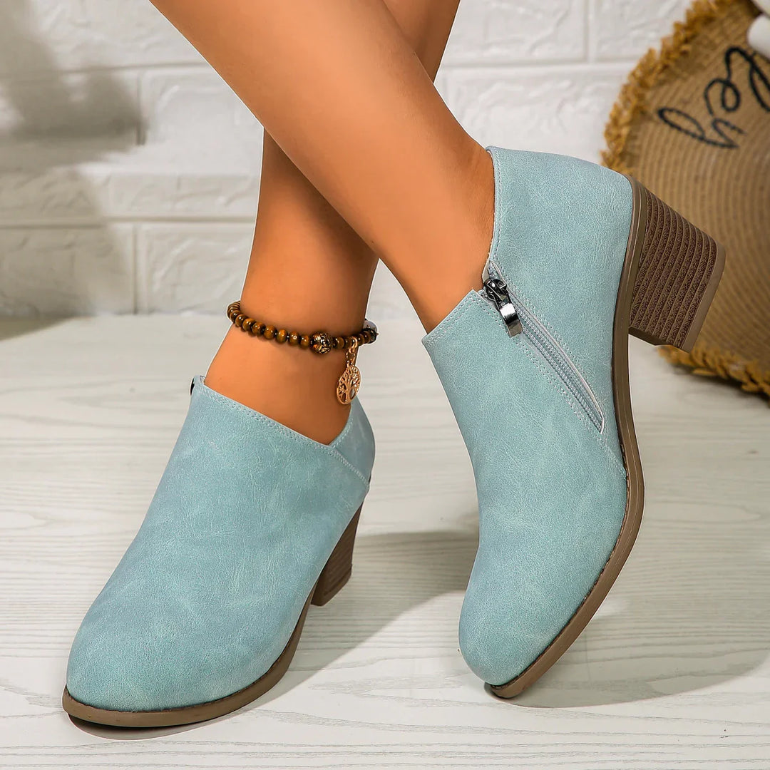 Light blue suede ankle boots with block heels and side zipper on wooden floor