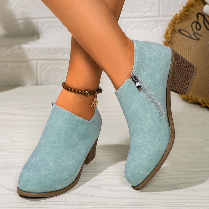 Light blue suede ankle boots with block heels and side zipper on wooden floor