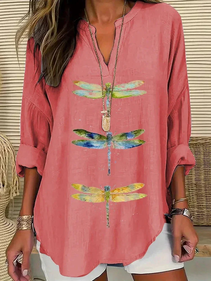 Woman wearing coral pink relaxed fit blouse with colorful dragonfly prints and rolled-up sleeves