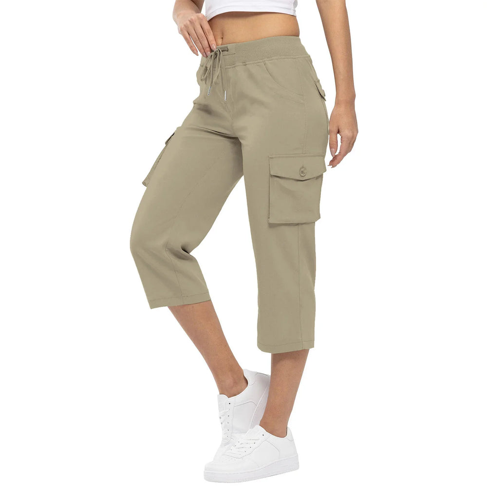 Woman wearing khaki cargo capri pants with drawstring waist and white sneakers on white background