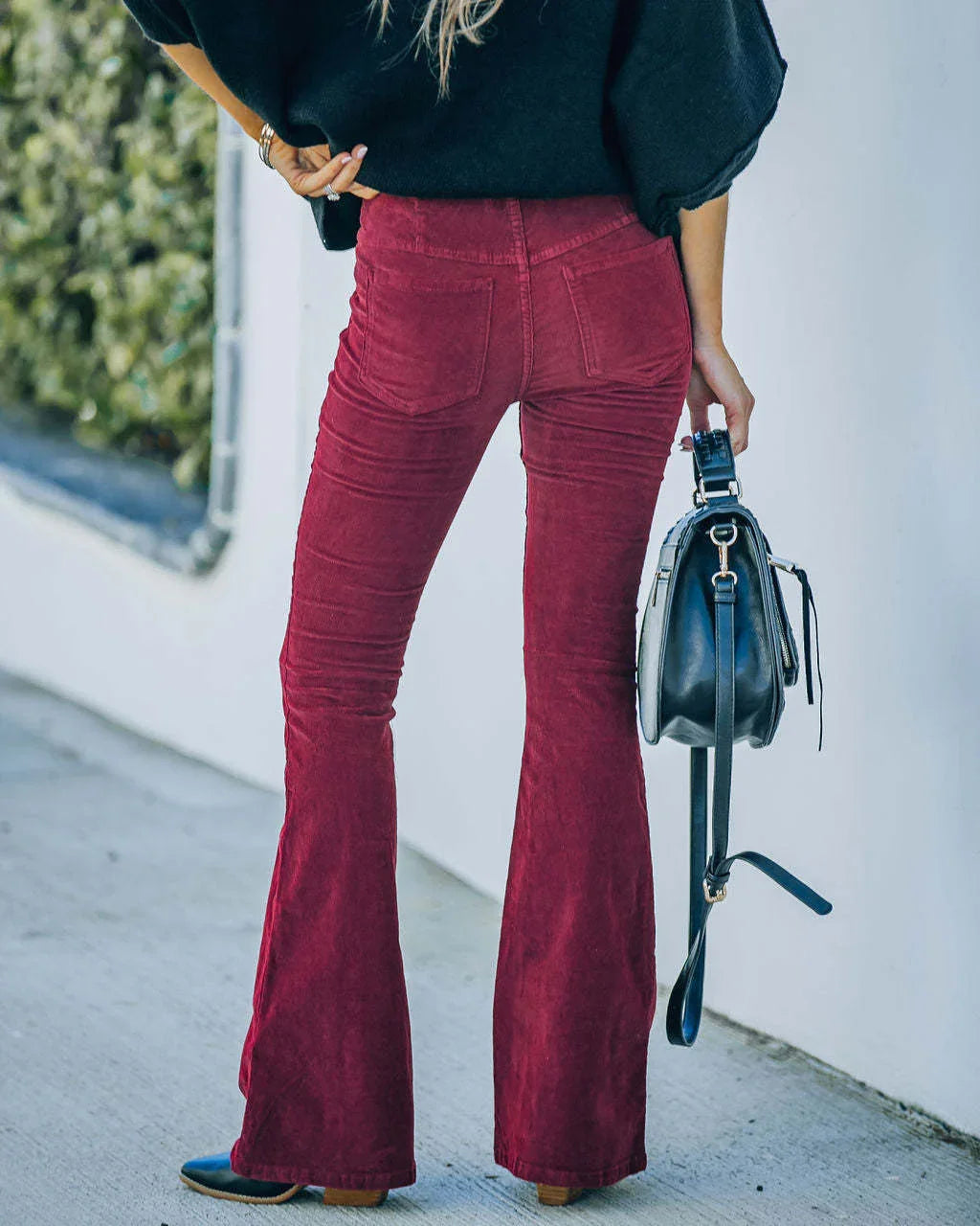 Woman wearing burgundy corduroy flare pants and holding black leather handbag outdoors