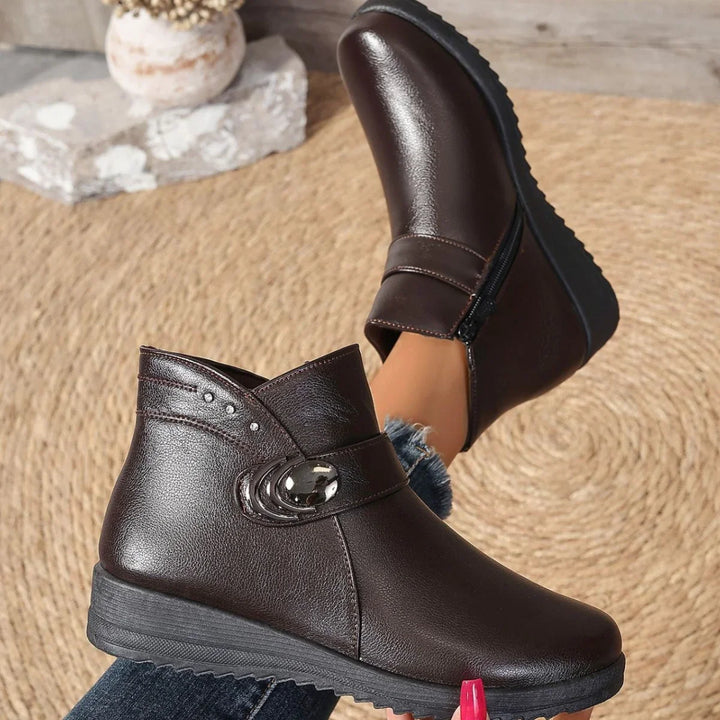 Women's brown leather ankle boots with decorative button and wedge soles on woven rug