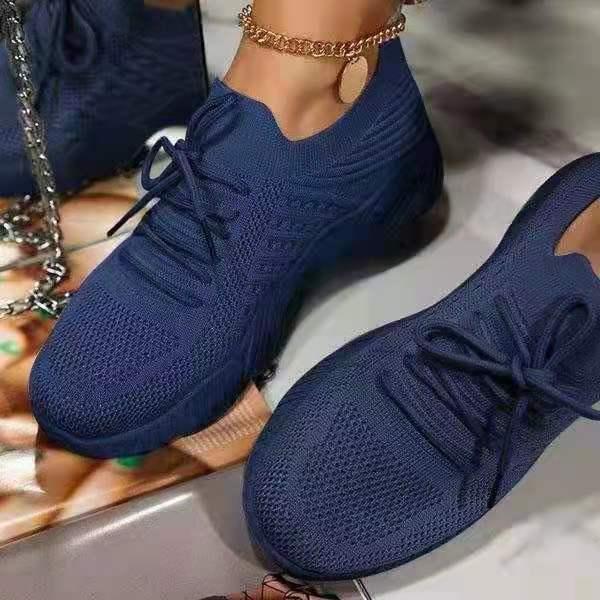 Close-up of navy blue knitted sneakers with laces worn with a gold anklet on a light surface