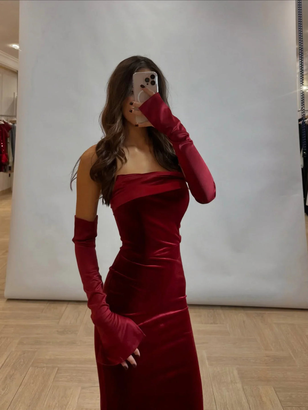 Woman in a fitted strapless red velvet dress with matching long gloves taking a mirror selfie