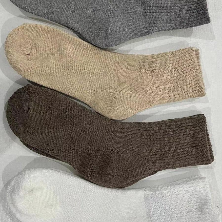 Four pairs of ribbed knit socks in gray, beige, brown, and white colors arranged on a white surface