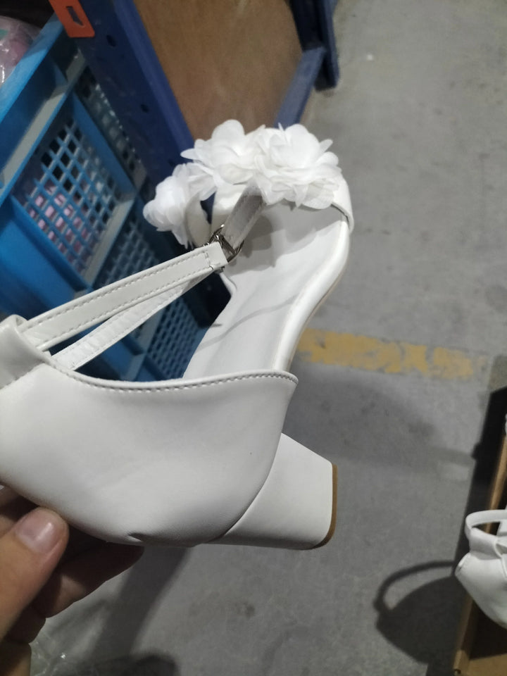 White block heel sandal with ankle strap and fabric flower decoration on gray floor