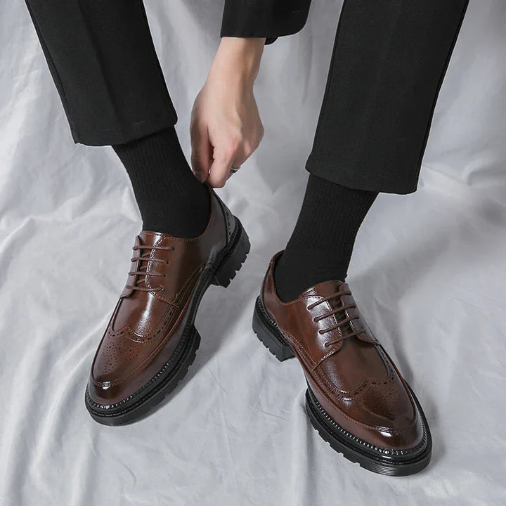 Man wearing polished brown leather brogue shoes with black soles and black socks, adjusting footwear