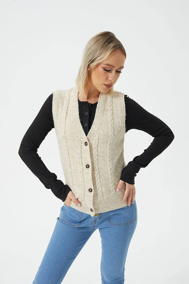 Woman wearing a cream cable knit buttoned vest over a black long sleeve top with blue jeans