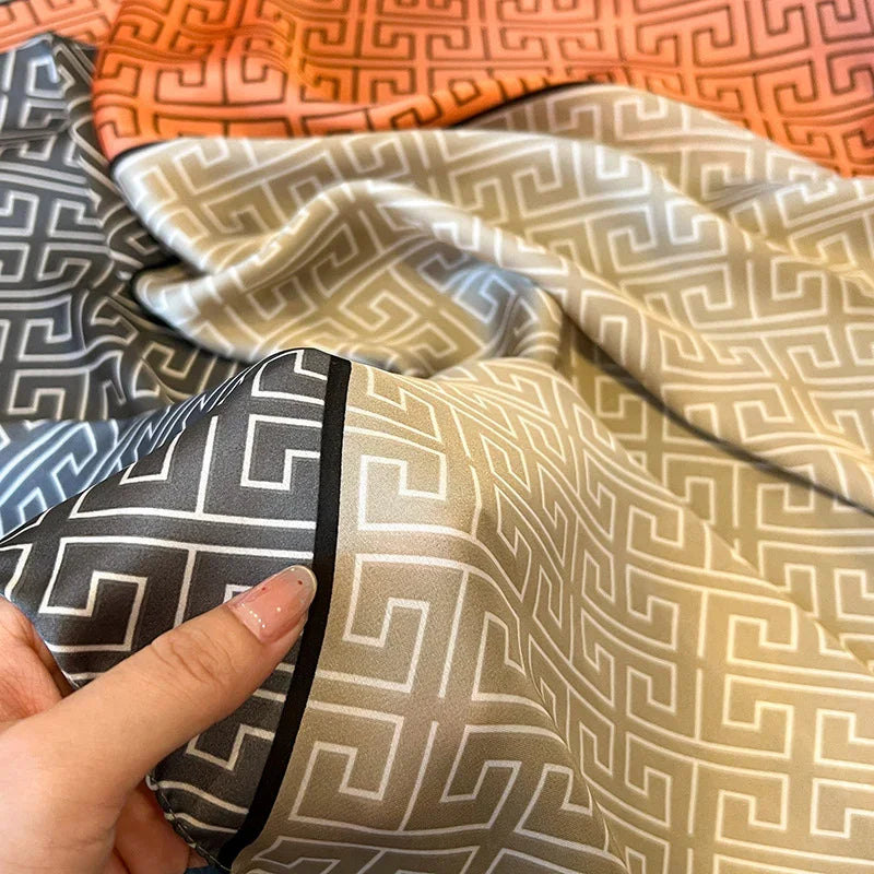 Close-up of hand holding silky fabric with geometric Greek key pattern in beige, gray, and orange colors