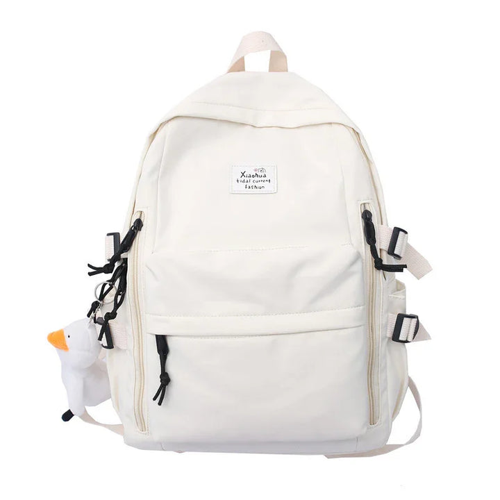 White backpack with front zipper pockets, black zipper pulls, side buckles, and a small plush duck keychain