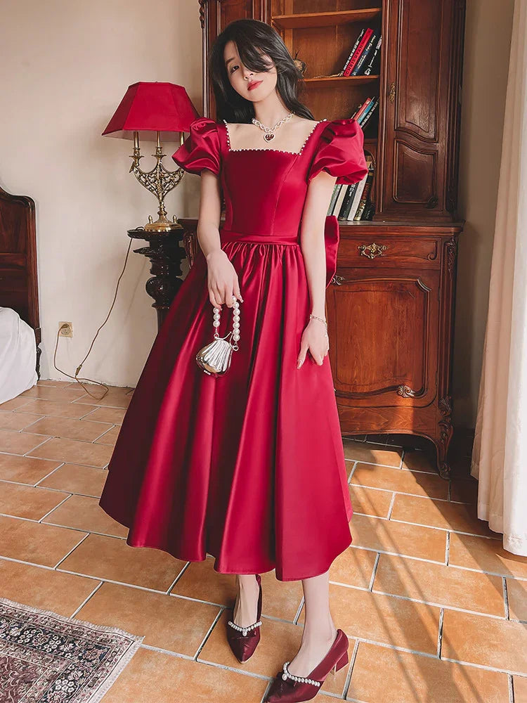 Woman wearing elegant red midi dress with puff sleeves and pearl-embellished shoes standing indoors