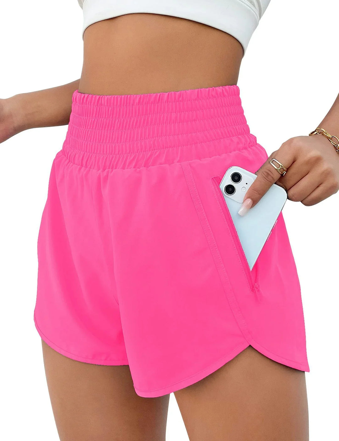 Woman wearing bright pink athletic shorts with high elastic waistband and zippered pocket holding smartphone