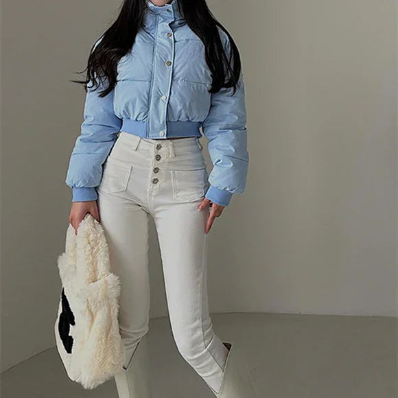 Woman wearing light blue cropped puffer jacket and high-waisted white pants holding fluffy tote bag