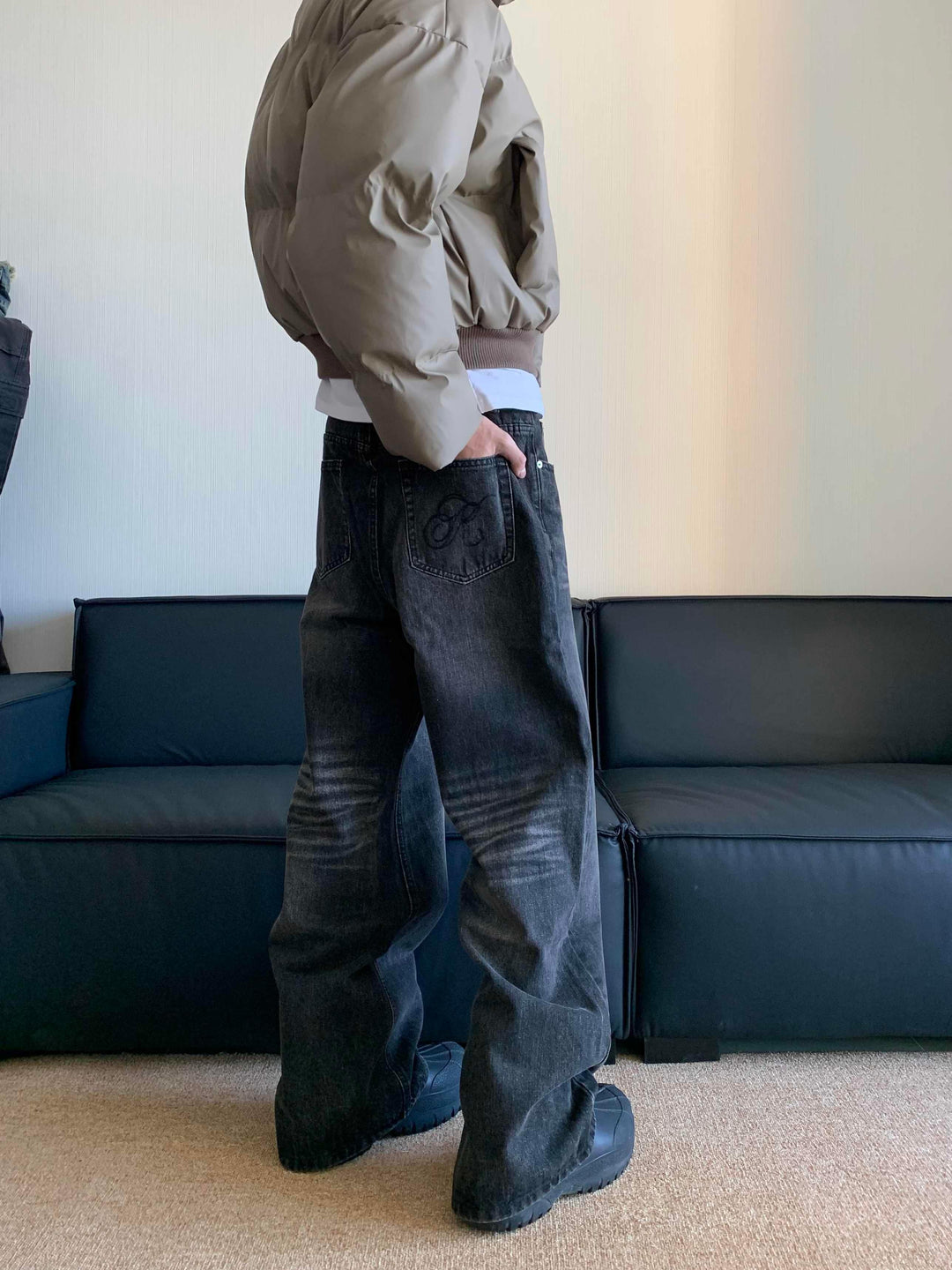 Person wearing beige puffer jacket and loose black jeans with embroidered back pocket standing indoors