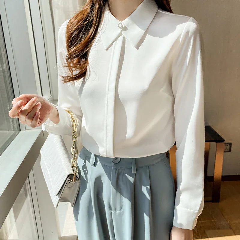 Woman wearing white collared blouse with pearl button and light blue high-waisted pants, holding white handbag