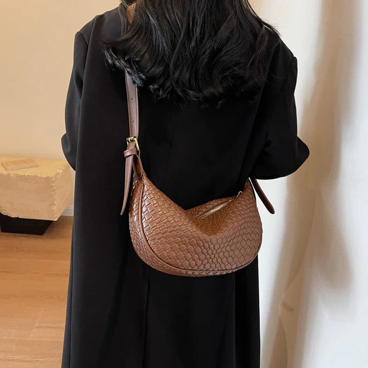 Brown woven leather shoulder bag worn crossbody on woman in black coat indoors