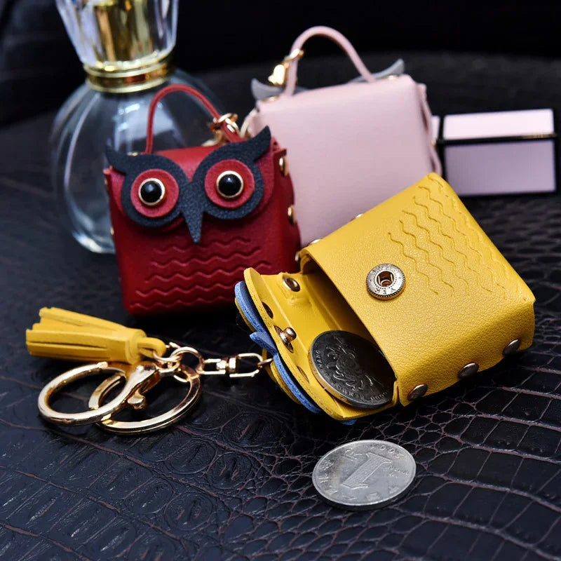 Compact leather coin purses with keyrings in yellow, red owl design, and pink on black textured surface