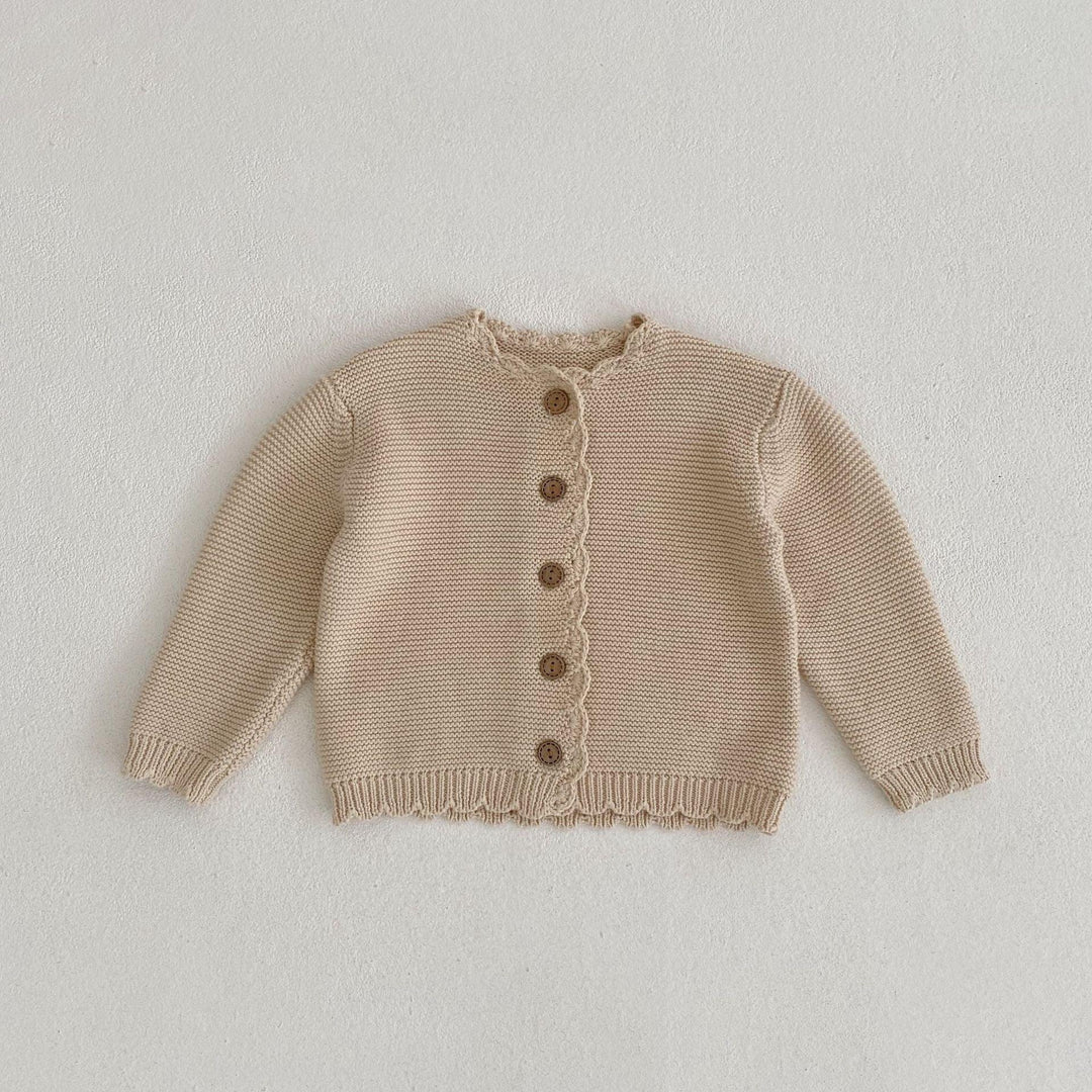 Beige knitted baby cardigan with wooden buttons on white textured background