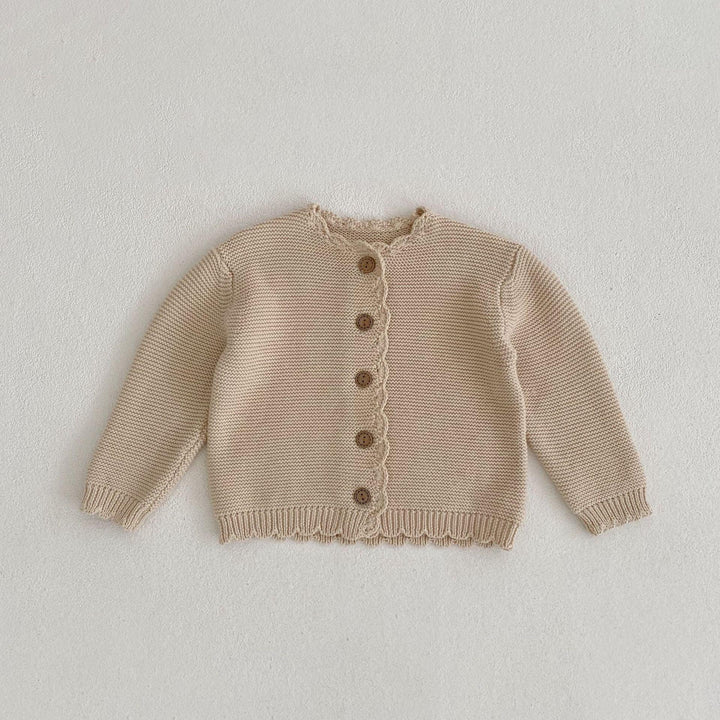 Beige knitted baby cardigan with wooden buttons on white textured background