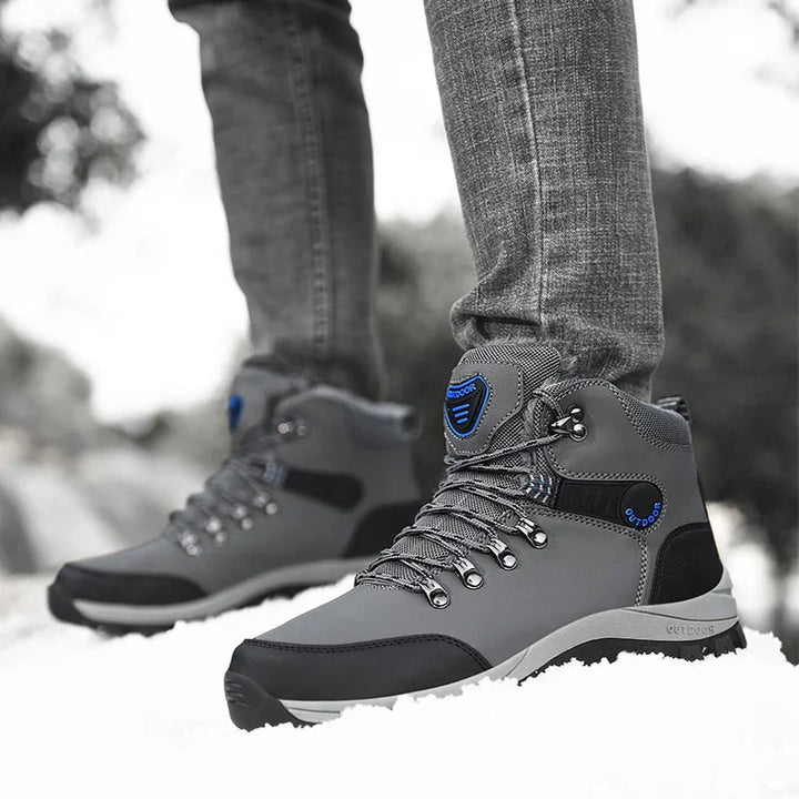 Gray and black outdoor hiking boots with blue accents worn with jeans on snow