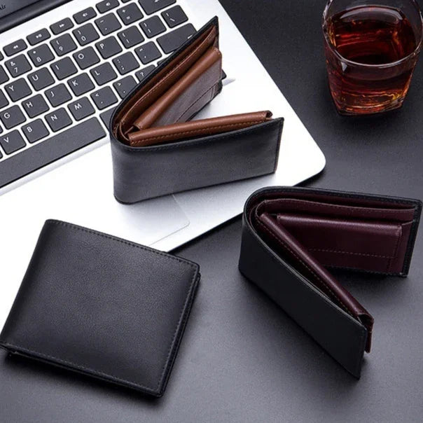 Black leather wallets displayed on a laptop keyboard and dark surface with a glass of brown liquid