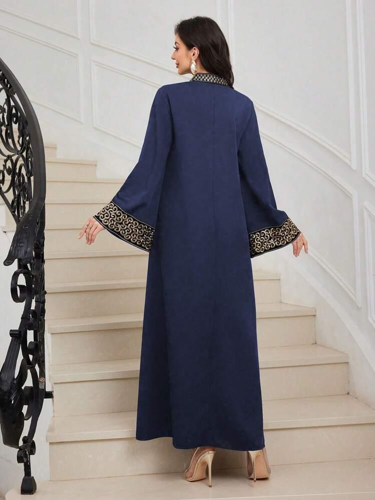 Woman in navy blue abaya with gold embroidered cuffs and collar standing on beige stairs