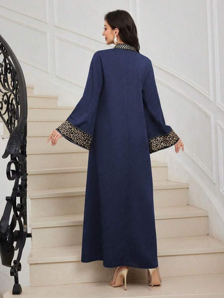 Woman in navy blue abaya with gold embroidered cuffs and collar standing on beige stairs