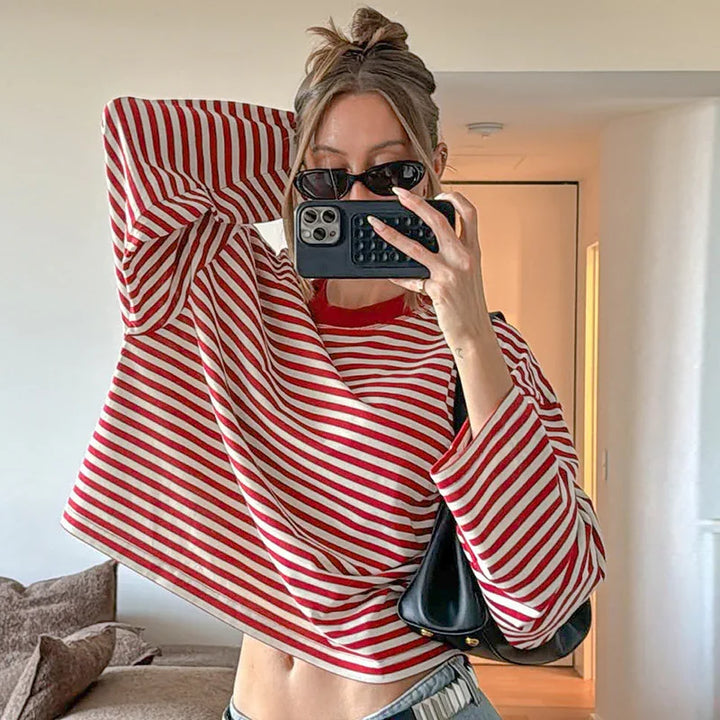 Woman wearing red and white striped long-sleeve shirt with sunglasses taking mirror selfie indoors