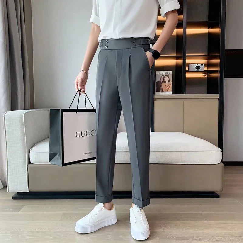 Person wearing gray pleated trousers and white sneakers holding a Gucci shopping bag in a modern living room