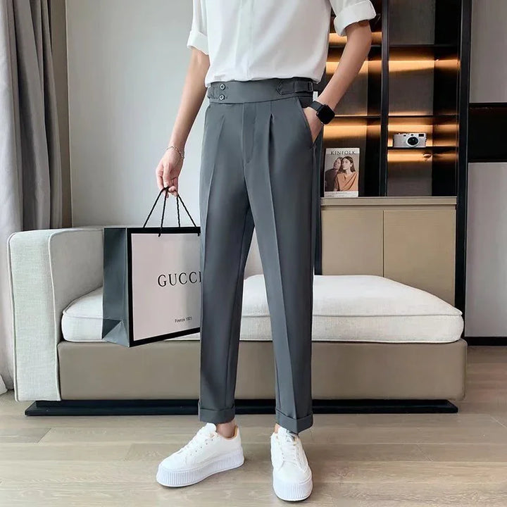 Person wearing gray pleated trousers and white sneakers holding a Gucci shopping bag in a modern living room