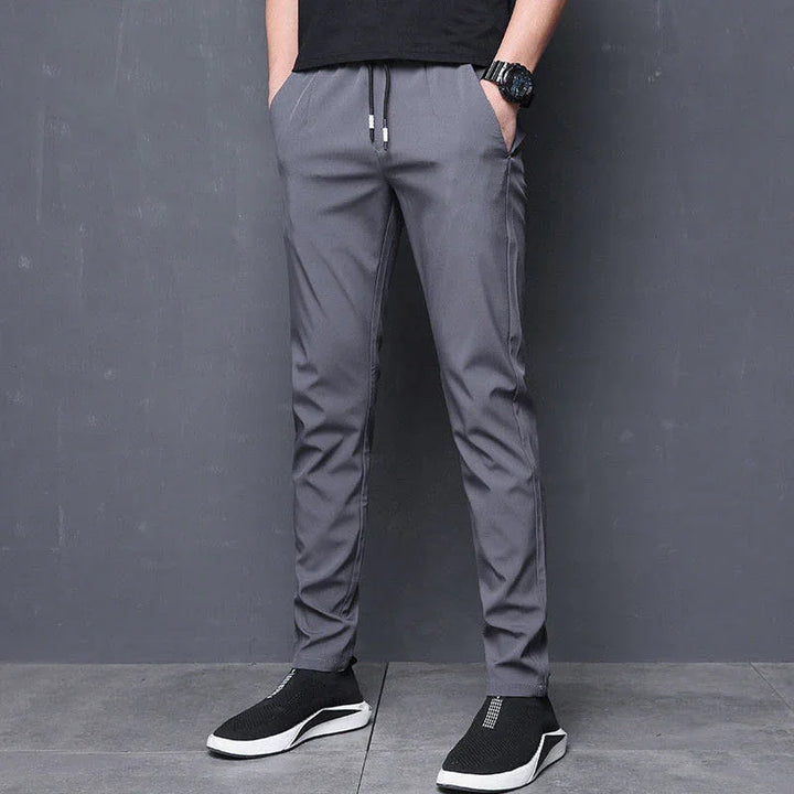 Man wearing gray slim-fit jogger pants with drawstring waist and black slip-on sneakers
