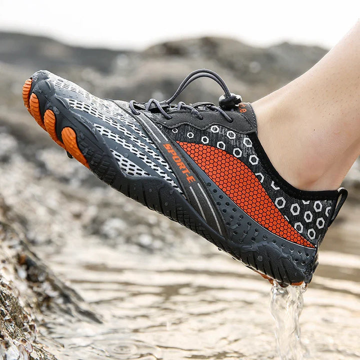Black and orange water sports shoe with honeycomb pattern draining water on rocky riverbank