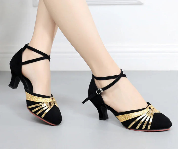Black suede women's dance shoes with gold metallic straps and low heels on light floor